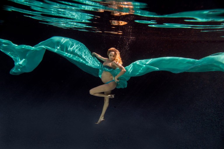 Pregnant woman underwater in long cyan flowy dress